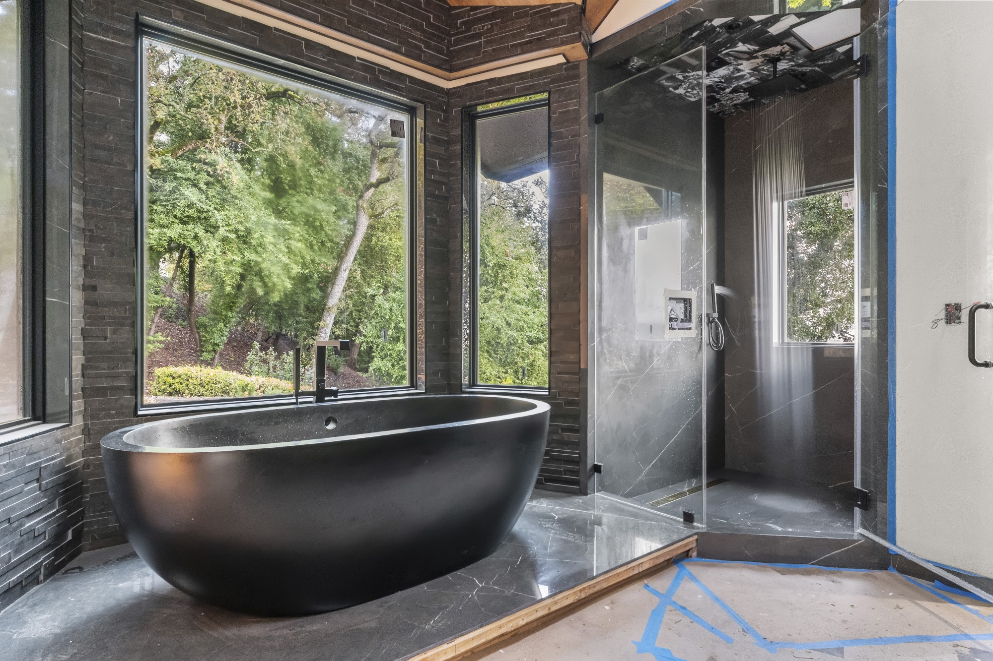 Finished bathroom with a dark freestanding tub and floor-to-ceiling windows